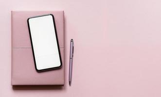 Draufsicht ein Smartphone-Modell auf einem Notizbuch und einem rosa Tisch