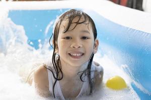 Schönes asiatisches Mädchen, das in einem aufblasbaren Pool spielt. im Sommer zu Hause im Wasser spielen. Seifenblasenspiel, Familienglück, im Wasser spielende Kinder foto