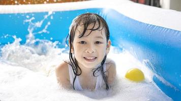 Schönes asiatisches Mädchen, das in einem aufblasbaren Pool spielt. im Sommer zu Hause im Wasser spielen. Seifenblasenspiel, Familienglück, im Wasser spielende Kinder foto