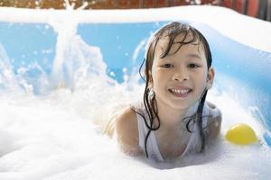 Schönes asiatisches Mädchen, das in einem aufblasbaren Pool spielt. im Sommer zu Hause im Wasser spielen. Seifenblasenspiel, Familienglück, im Wasser spielende Kinder foto