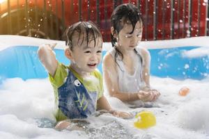 Der süße kleine Junge und die Schwester haben Spaß beim Spielen mit Blasen und bunten Bällen im aufblasbaren Pool. aufblasbare und Sprudelbecken, Schwimmen im Sommer, fröhliche Kinder, die im Wasser spielen foto