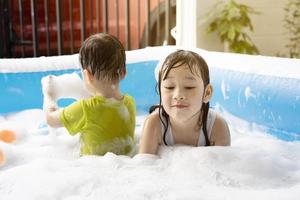 schwester und bruder haben spaß beim spielen mit blasen im schwimmbad zu hause. Sommerwasserspiel, Familienglück, Kinderglück foto