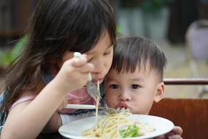 asiatische Jungen und Mädchen essen Spaghetti mit Köstlichkeit. Schwester und Bruder essen Spaghetti foto