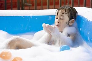 Schönes asiatisches Mädchen, das am Wochenende mit Blasen in einem aufblasbaren Swimmingpool spielt. schönen Familienurlaub. Kinder spielen im Pool. foto