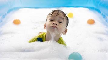 Süßer kleiner asiatischer Junge, der in Blasen in einem aufblasbaren Pool schwimmt. Sommerwasserspiel, Familienglück, Kinderglück, Pool und bunte Bälle foto