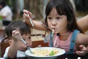 asiatische Jungen und Mädchen essen Spaghetti mit Köstlichkeit. Schwester und Bruder essen Spaghetti foto