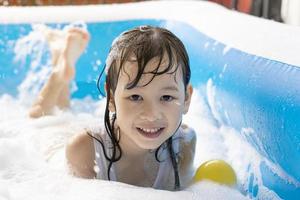 Schönes asiatisches Mädchen, das in einem aufblasbaren Pool spielt. im Sommer zu Hause im Wasser spielen. Seifenblasenspiel, Familienglück, im Wasser spielende Kinder foto