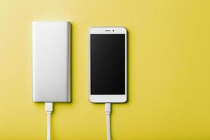 Smartphone aufladen mit Powerbank per Kabel auf gelbem Hintergrund. foto