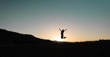 Mädchen springt bei Sonnenuntergang in den Bergen foto