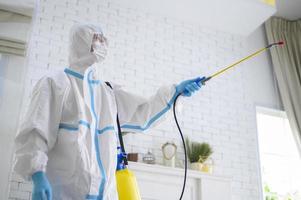 Ein medizinisches Personal im Anzug verwendet Desinfektionsspray im Wohnzimmer. foto