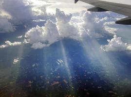 Luftaufnahme, die über dramatischen, flauschigen Wolken und Sonnenstrahlen fliegt, die durch die Wolken stechen, sonnige Wolkenlandschaft, Sonnenlicht, Flugreisen, Teil des Flugzeugs, Flügel
