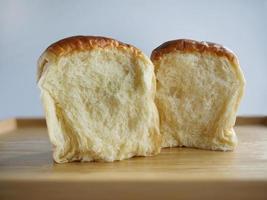 Nahaufnahme zeigt den Querschnitt, 2 Brötchen frisch gebackenes japanisches Hokkaido weiches und flauschiges Milchbrot, japanische Brioche auf dem Holztablett mit einfarbigem Hintergrund, gelber Ton foto