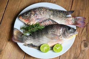 Tilapia mit weißer Platte mit Rosmarin-Zitronenkalk auf Holzhintergrund, frischer roher Tilapia-Fisch von der Tilapia-Farm foto