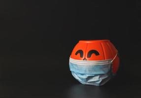 Halloween-Kürbis aus Kunststoff mit medizinischer Gesichtsmaske isoliert auf schwarzem Hintergrund mit Kopierraum. neues normales halloween-konzept foto