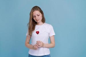 junge Frau hält rotes Herz auf Stick in weißem T-Shirt auf blauem Hintergrund. foto