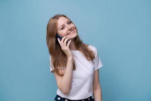 Fröhliche kaukasische junge Frau, die am Telefon auf blauem Hintergrund spricht, mobil foto