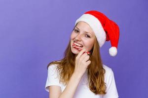 junge Frau in Weihnachtsmütze isst Lutscher Lutscher auf Flieder im weißen T-Shirt. foto