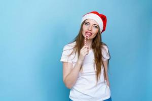 junge Frau im weißen T-Shirt mit Weihnachtsmütze auf blauem Hintergrund. süßer Weihnachtsmann foto