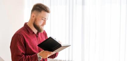 bärtiger mann des geschäfts steht im büro gegen fenster und schreibt pläne auf foto