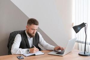 gutaussehender geschäftsmann arbeitet mit laptop im büro, in geschäftskleidung foto