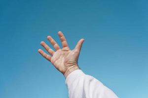 Hand in die Luft gestikulierend in den blauen Himmel, blauer Hintergrund foto