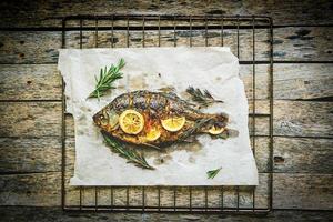 gekocht auf pergamentpapier, gebackener fisch mit gewürzen, zitrone und rosmarin.barbecue grill auf einem hölzernen hintergrund. foto