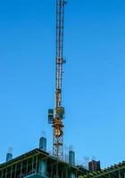 Baukran gegen den blauen Himmel. die Immobilienbranche. Ein Kran verwendet Hebezeuge auf einer Baustelle. foto