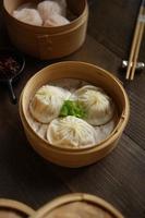 vertikale ansicht von xiao lung pao dimsum im bambuskorb, auf dem holztisch. foto