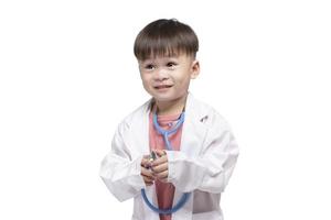 Junge trägt einen Arztanzug mit einem medizinischen Stethoskop auf weißem Hintergrund. Kinder im Vorschulalter geben sich als Kinderarzt aus. Kindheitstraum, Arzt zu werden foto