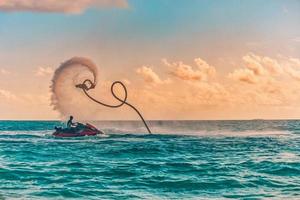 Silhouette eines Flyboard-Fahrers auf See. Berufsreiter machen Tricks in der blauen Lagune. tropische Wassersportausrüstung. sonnenuntergang meerblick, sommersport im freien, freizeitaktivität, tolles spritzen foto