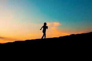 die Silhouette eines Mädchens, das auf einem Hügel am Sonnenuntergangshimmel läuft foto
