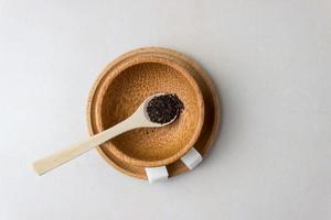 Zwei Zuckerwürfel in einem Holzteller und Löffel mit Teeblättern auf dem Küchentisch. Tee kochen, Teepause. Ansicht von oben foto