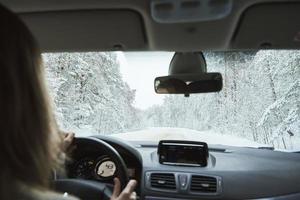 verschneite Straße im Winterwald mit fahrendem Auto foto