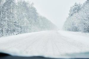 verschneite Straße im Winterwald mit fahrendem Auto foto