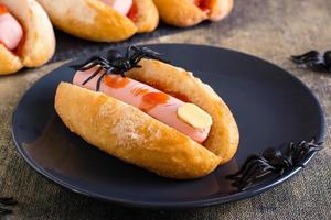 ein amputierter Wurstfinger in Ketchup in einem Brötchen auf einem Teller. Halloween-Rezept. foto
