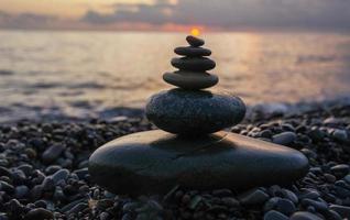 Pyramide aus Kieselsteinen mit Sonne an der Spitze vor dem Hintergrund des Meeres und des Sonnenunterganghimmels. Zen-Steine, Meditationskonzept foto