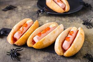 Hot Dogs aus Wurst und Käse in Ketchup im Brötchen auf Schiefer. Halloween-Rezept foto