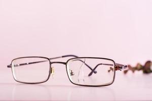 Alte Brille mit zerbrochener Linse und einem Draht, der am Bügel auf rosafarbenem Hintergrund befestigt ist foto