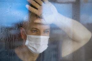 Porträt eines Mannes mit Schutzmaske blickt durch die Fenster auf die Straße foto