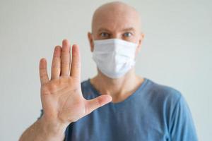 ein glatzköpfiger mann hält eine medizinische maske in den händen, die andere hand streckt er aus protest aus foto