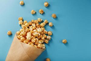 Popcorn in Karamellglasur in einem Papierumschlag auf blauem Hintergrund. foto