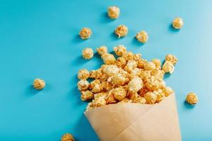 Popcorn in Karamellglasur in einem Papierumschlag auf blauem Hintergrund. foto