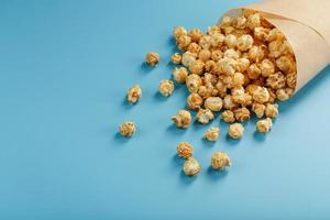 Popcorn in Karamellglasur in einem Papierumschlag auf blauem Hintergrund. foto