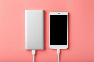 powerbank lädt ein smartphone auf einem rosa hintergrund auf. Universelle externe Batterie für Gadgets Freiraum und minimalistische Komposition. foto