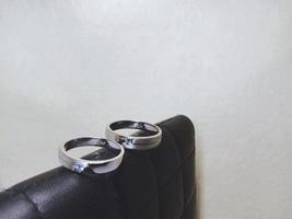 Ein Paar Eheringe und Verlobungsringe mit silbernem Material auf einer schwarzen Brieftasche auf weißem Hintergrund foto