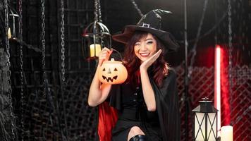 fröhliches halloween, junge asiatische frau im schwarzen kostüm, das hexenhut trägt, der laternenkürbis trägt. Emotion Lächeln foto