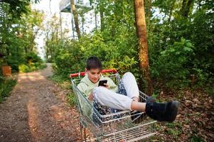 Junge sitzt im Trolley mit Handy im Wald. foto