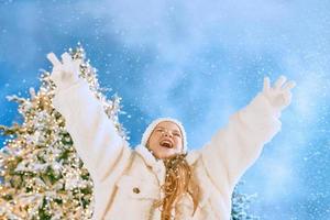 süßes kaukasisches blondes mädchen in weißem öko-pelzmantel, hut und handschuhen glücklich im winter. neujahr, weihnachten, märchen, modekonzept foto