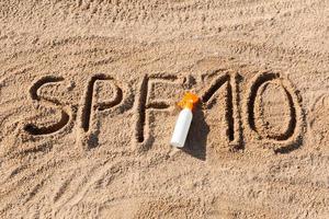 Sonnenschutzfaktor zehn. spf 10 wort geschrieben auf dem sand und der weißen flasche mit sonnencreme. hintergrund des hautpflegekonzepts foto
