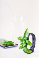 frische Blätter auf dem Bildschirm eines Fitnessarmbandes, auf einem Smartphone und einem Glas Wasser. das konzept der gesundheitsversorgung, vitalität. vertikale Ansicht foto